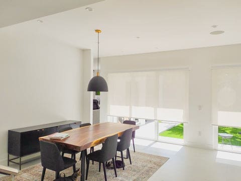 White solar shades in dining room with wooden table, black chairs and beige rug